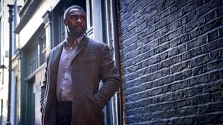 John Luther stands stoically in an alleyway in Luther: The Fallen Sun