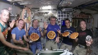 Astronauts and cosmonauts show off their pizza creations on the International Space Station in this still from a video by the station's Expedition 53 crew. They are (from left): NASA astronaut Mark Vande Hei; Russian cosmonauts Sergey Ryazanskiy and Alexander Misurkin; European Space Agency astronaut Paolo Nespoli and NASA astronauts Joe Acaba and Randy Bresnik.