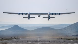 A dual-fuselage aircraft lifts off carrying a test vehicle