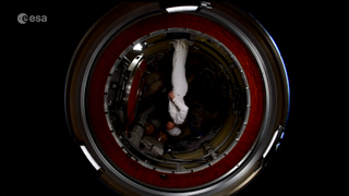 astronaut samantha cristoforetti upside down in a space station module in a white suit