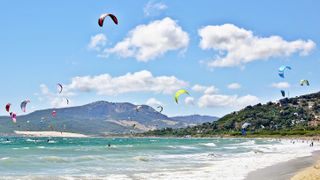 tens of kite surfers out on the water as the sea crashes on to the beach.