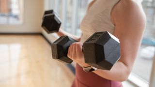 Person holding two dumbbells during bicep curl close up