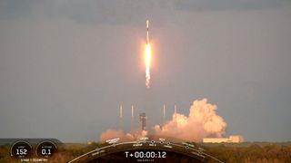 a black and white spacex rocket launches into a darkening evening sky