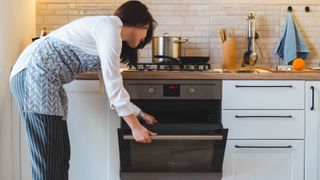 Someone leaning into an open oven while wearing an apron