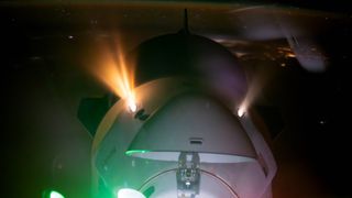 A SpaceX Dragon spacecraft fires its thrusters under green and red lights with a nighttime Earth in the background while docking.