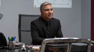 Nick Mohammed as Nate in a black suit sitting at his desk in Ted Lasso.