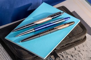 three pens sit on a light-blue notebook on a table.