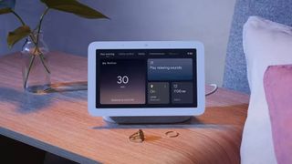 Google Nest Hub 2nd Gen on a bedside table next to some pillows.