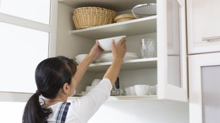 Woman storing plates in kitchen cabinet