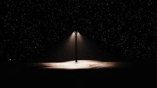 An artist's rendering of a streetlamp on a dark landscape with stars behind it