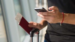 Man at airport terminal holding passport, ticket and phone