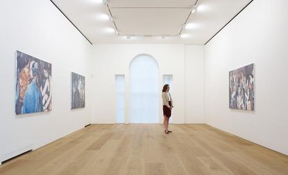 Art exhibition space with white walls. A lady stands looking at one of the three pieces of artwork.