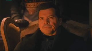 John Leguizamo sitting down in a dimly lit room in Violent Night 