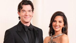 John Mulaney and Olivia Munn in a suit and dress on the red carpet, 2024.