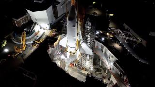 a space shuttle wrapped in white plastic stands upright surrounded by buildings