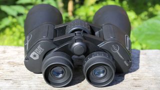 Celestron EclipSmart 12x50 porro solar binoculars placed on a wooden surface with green foliage behind