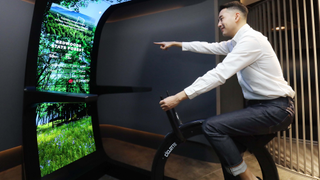 Man on fitness bike looking at LG Display Virtual ride, an emcompassing screen structure featuring flexible LG OLED panels.