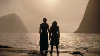 Silhouettes of a man and woman standing side by side, looking off into the sunset over the water. 
