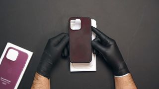 A dirty iPhone 15 FineWoven case on a table, held by someone wearing rubber gloves
