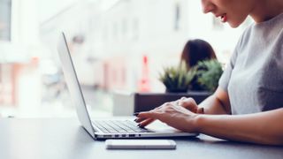 A woman sitting at a table, working on a MacBook laptop