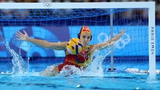 Spain's Martina Terre, leaps to save a penalty, in a red swimsuit, in the water polo at the 2024 Paris Olympic Games.