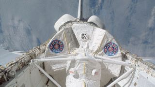 Earth can be seen behind the open bay of a white space shuttle