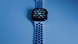 The Apple Watch Series 7 pictured on a pale blue surface displaying the app menu