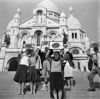 a group of seven people stand on steps and hold frame structures above their heads with projections of the sun on.