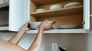 A woman stacking crockery in a cupboard