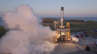 fire and smoke spew from a sliver cylinder upright on a large metal platform