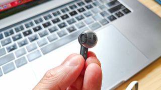 Reviewer holding a single Amazon Echo Bud with keyboard in the background