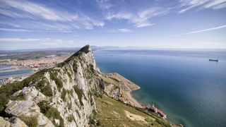 aerial view of Gibraltar rock in the foreground and a vast body of water in the background with a partly cloudy sky above.