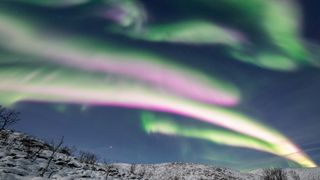 Pink auroras shimmering above the Arctic landscape in Norway.