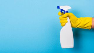 An unlabelled spray bottle being held by a gloved hand on a blue background