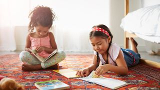 Two young girls lying on the floor reading science books