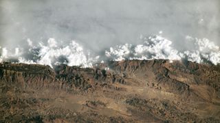 A satellite photo of a wall of haze and cloud trapped behind a mountain range