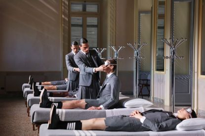 Thom Browne Frette Homeware Milan Design Week 2024 presentation: models in grey suits lie on beds