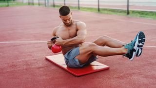 Man performing ab workout on mat outdoors showing a kettlebell Russian twist