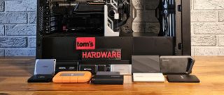 Recent extneral SSDs in front of our storage testbed, with 3D-printed Tom&#039;s Hardware logo