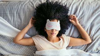 A woman lies in bed sleeping with an eye mask on