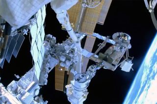 an astronaut in a spacesuit adjusts his visor outside the international space station with the curve of earth in the background