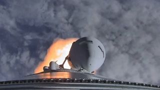 a large white rocket lifts off through a cloudy sky above a massive plume of fire and smoke