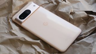 Google Pixel 8 i hvid ligger på et sammenkrøllet lysebrunt papir med bagsiden af mobiltelefonen vendt opad.