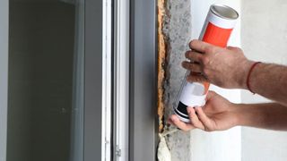 Someone filling the gap between a window and wall with insulation foam