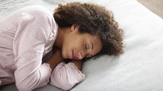 A woman with dark curly hair sleeps on her side in a pink nightdress