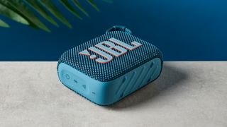 A photo of the JBL Go 4 in blue on a concrete surface against a blue wall.