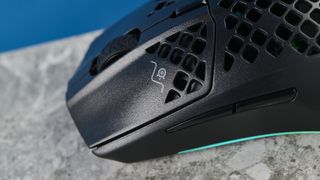 The SteelSeries Aerox 3 on a stone surface and wooden table against a blue background.