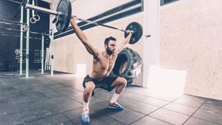 Man performing a snatch exercise holding a barbell in an overhead squat position in a gym