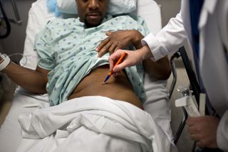 A doctor marks on a Black male patient which kidney to remove for a donation