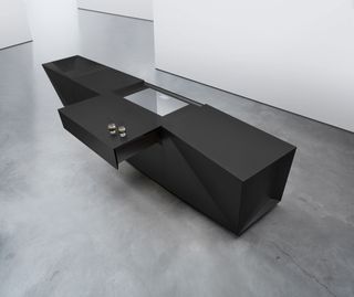 An aerial view of a rectangular black kitchen island on a concrete floor with white walls